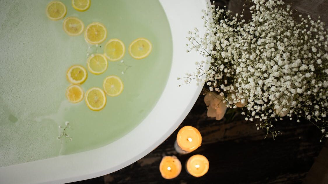 Round bathtub filled with water and floating lemon slices, surrounded by candles and flowers